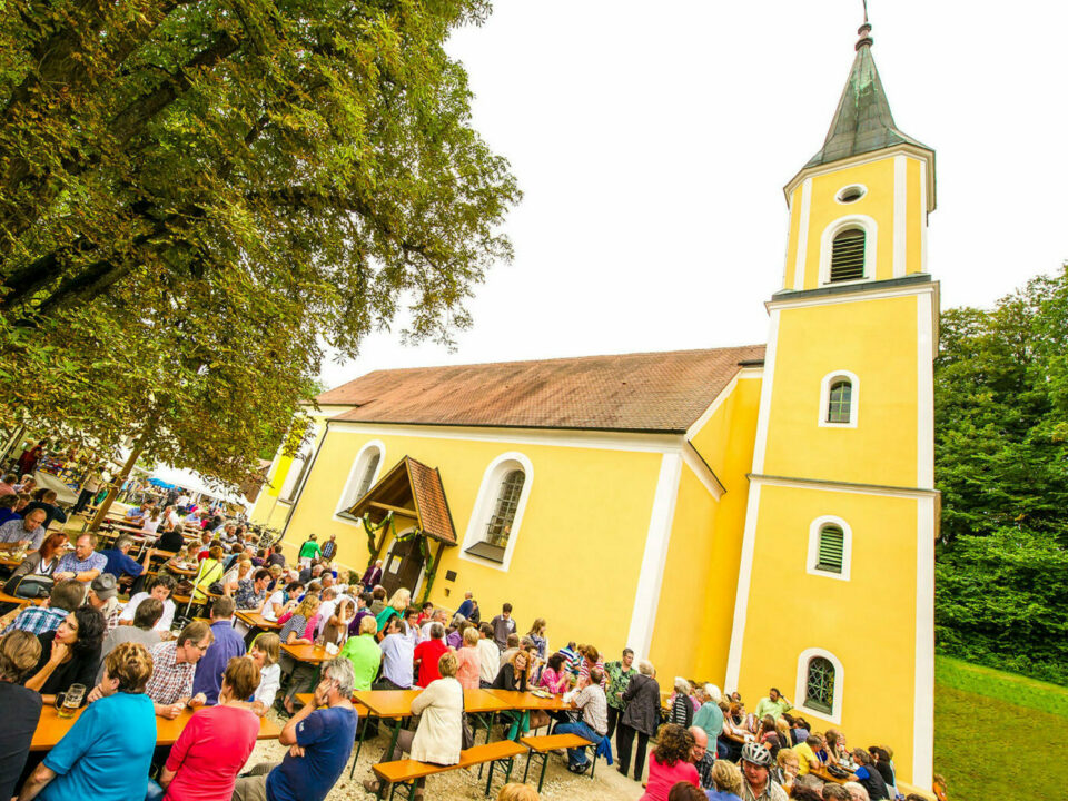 Mausbergkirche mit zahlreichen Menschen auf Bierbänken