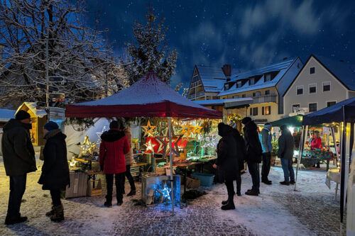Weihnachtsmarkt - Besucher stehen vor Buden und unterhalten sich