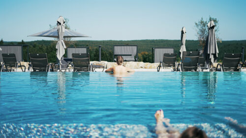 Frau im Pool schaut auf einen Wald