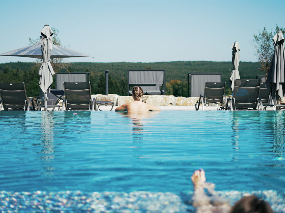 Frau im Pool schaut auf einen Wald